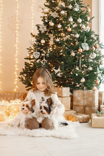 Little girl sitting near Christmas tree with two yorkshire terriers