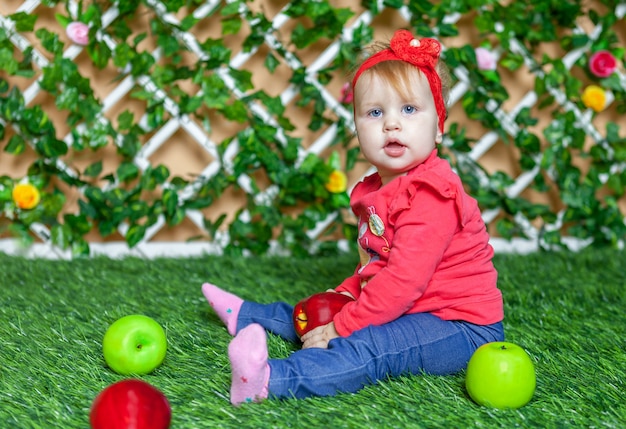 Little girl sitting in the park on the grass in sunny summer day and playing with apples.