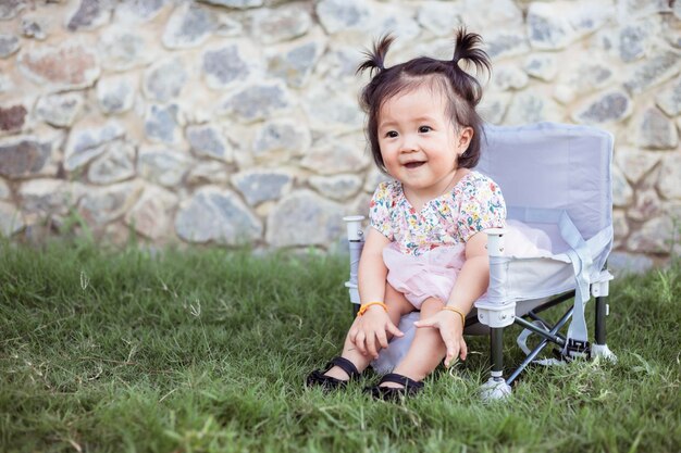 Little girl sitting on picnic chair in park in outdoor vacation summer Beautiful girl cute daughter travel camping in the garden Image of cute little girl