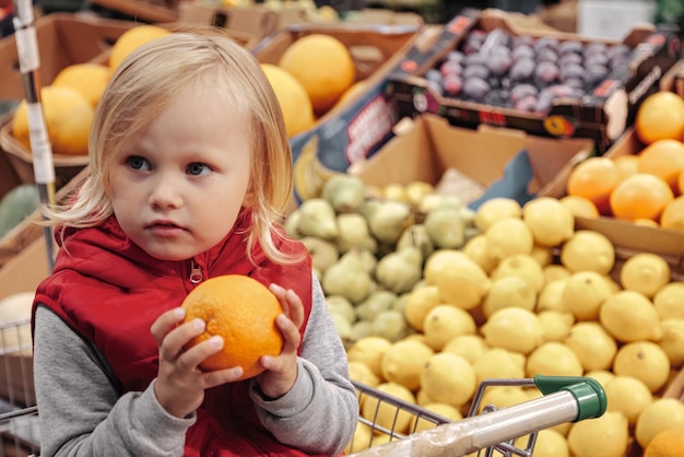 Little girl sitting in shopping cart in food fruit store or supermarket