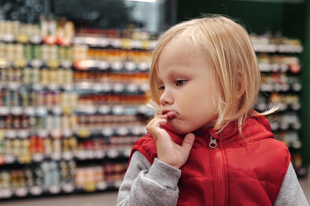 Little girl sitting in shopping cart in store or supermarket and buying