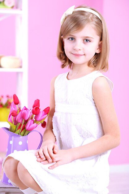 Little girl sitting on small ladder with flowers on pink background