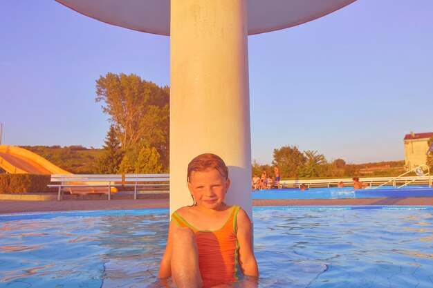 Little girl sitting under a sprinkler shower in swimming pool portrait of little cute girl in the