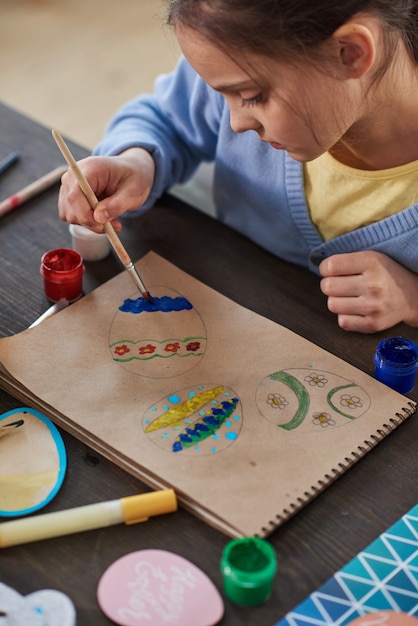 Little girl sitting at the table and drawing picture during art classes