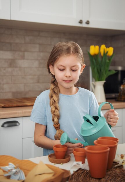 家のテーブルに座っている少女が植木鉢に種を蒔く家の園芸