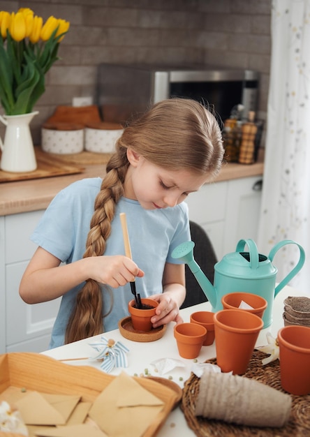 家のテーブルに座っている少女が植木鉢に種を蒔く家の園芸