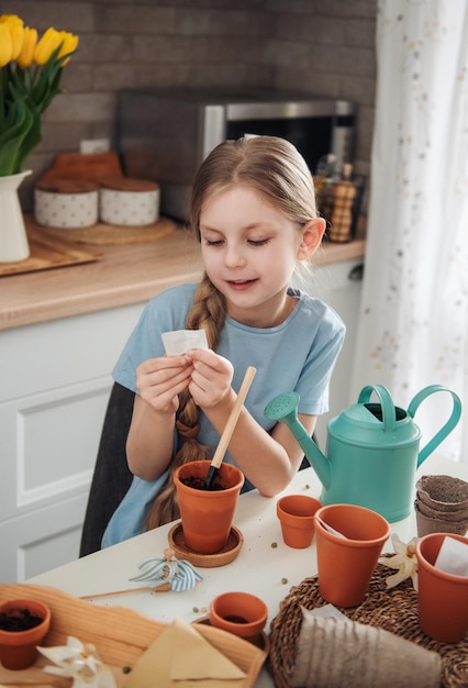 家のテーブルに座っている少女が植木鉢に種を蒔く家の園芸
