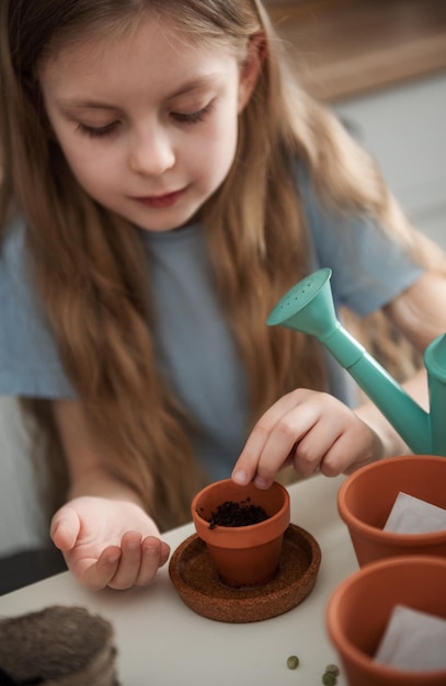 家のテーブルに座っている少女が植木鉢に種をまく