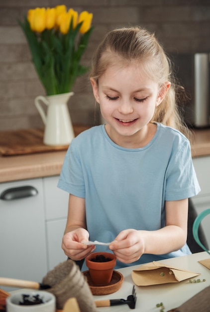 Little girl sitting at the table at home sowing seeds into flower pots