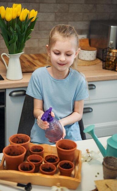 家のテーブルに座っている少女が植木鉢に種をまく