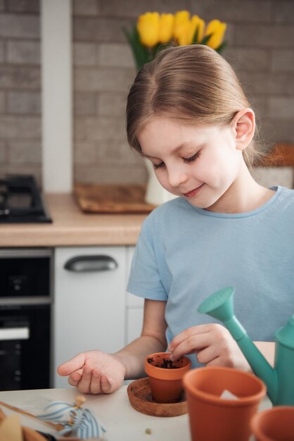 Little girl sitting at the table at home sowing seeds into flower pots