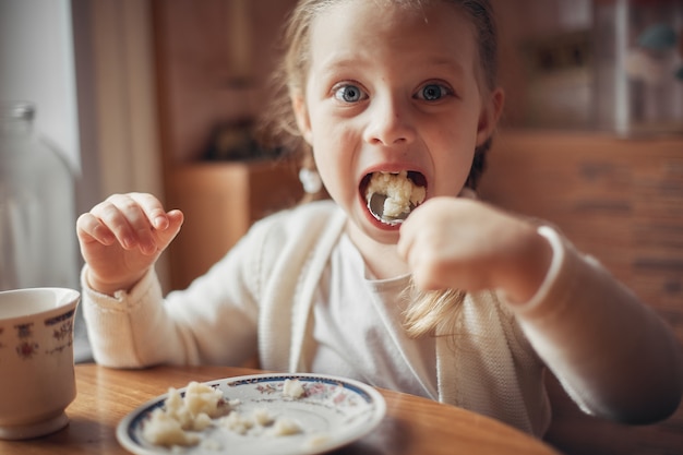 Foto una bambina seduta a un tavolo in cucina e mangiare porridge