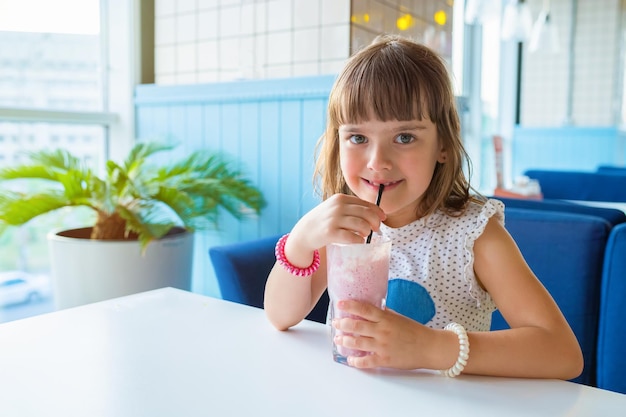 Little girl sitting at a table in a restaurant with a milkshake in her hands