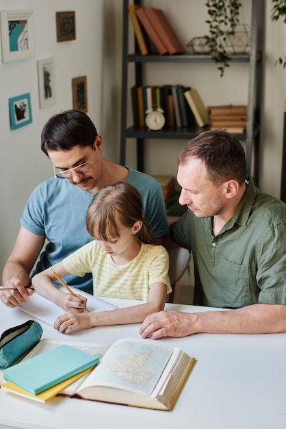 Little girl sitting at the table and studying with her parents teaching her they studying at home