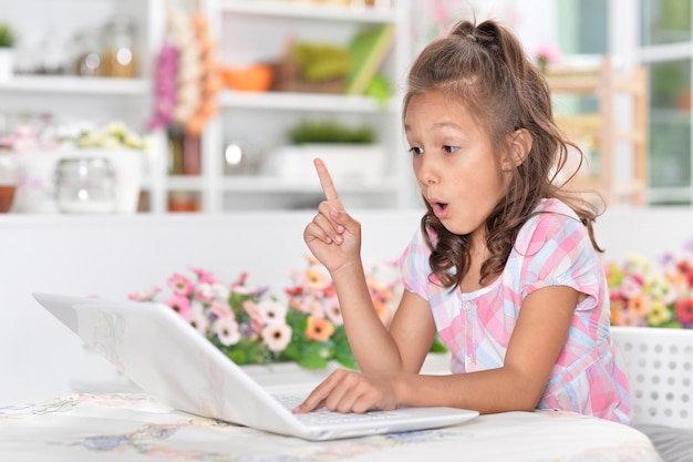 Little girl sitting at table and using modern laptop