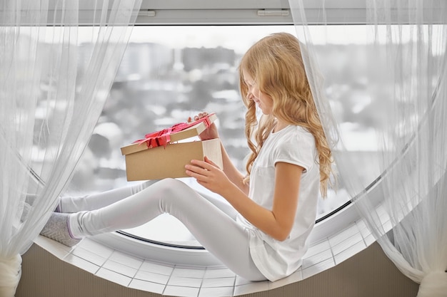 Little girl sitting on window and looking at present