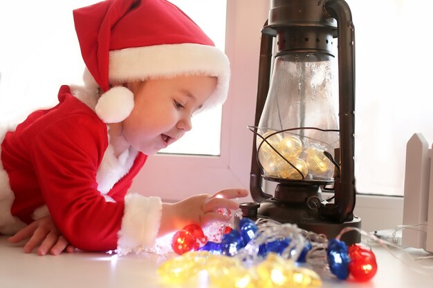 Little girl sitting on a window sill in a suit of Santa Claus