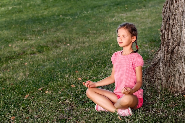 Little girl sitting in a yoga pose on the grass