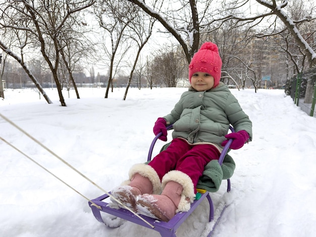 Фото Маленькая девочка катается на санях зимой.