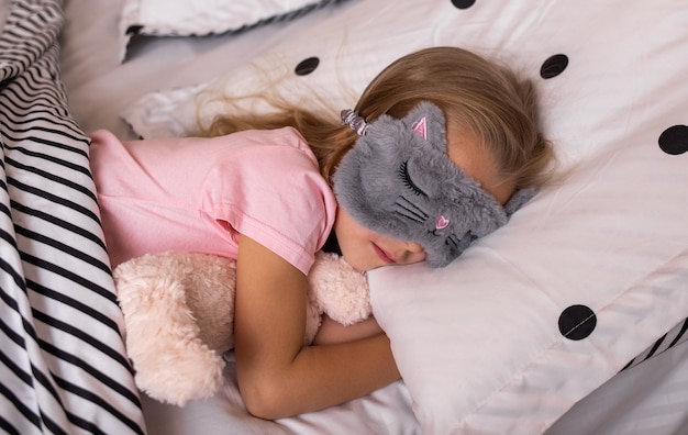 A little girl in a sleep bandage sleeps on cotton bedding in a bed in the bedroom