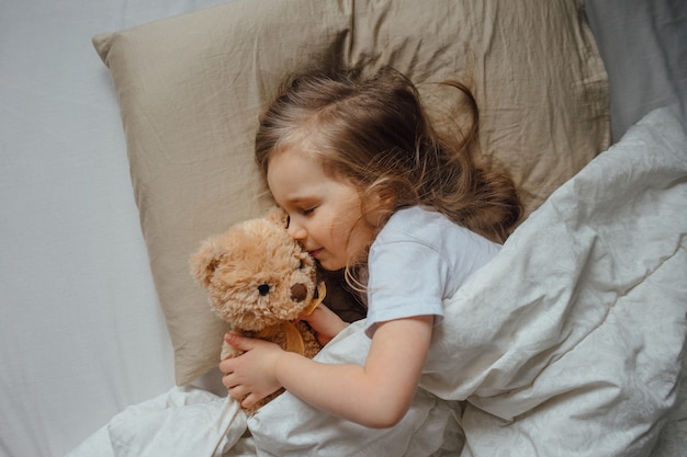 Foto bambina che dorme nel letto abbracciando il peluche a casa, vista dall'alto