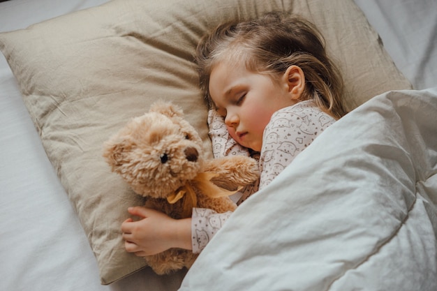 사진 집에서 부드러운 장난감을 안고 침대에서 자고 있는 어린 소녀, 위쪽
