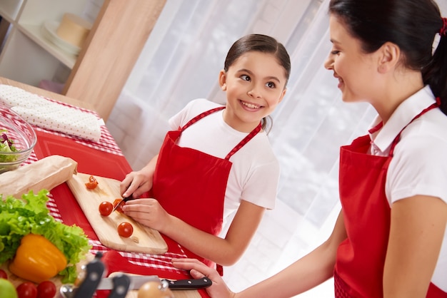 Little girl slicing tomatoes in the kitchen.