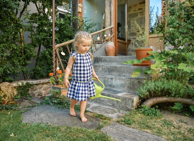 Piccola ragazza in un piccolo giardino con una pentola d'irrigazione verde