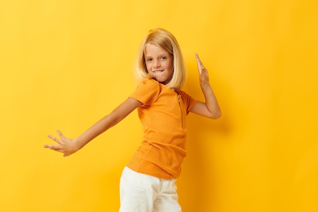 小さな女の子の笑顔の手のジェスチャーは、カジュアルな服装の楽しい黄色の背景を変更せずにポーズをとる