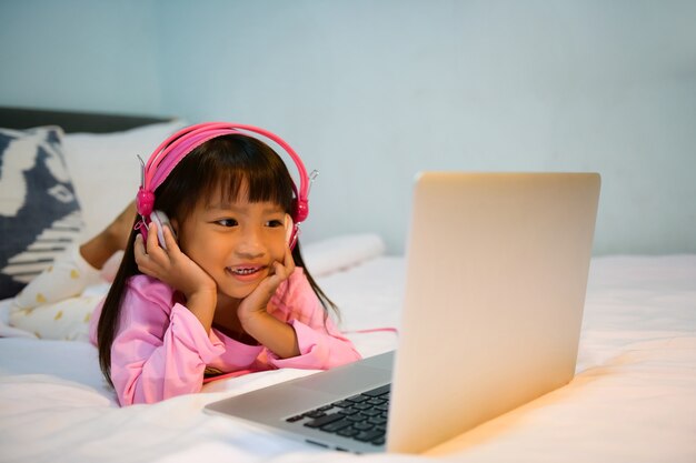어린 소녀는 행복한 미소를 지으며 매트리스 위에 노트북에서 Sao Bao의 노래를 들으며 누웠습니다.