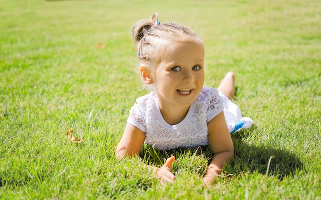 The little girl smiles playfully lying on the grass.