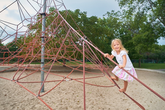 Little girl smiling looking, little child playing on climbing net . outdoors on sunny summer day.