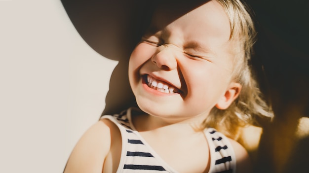 Foto bambina che sorride e strizza gli occhi alla luce del sole bambino felice che si diverte