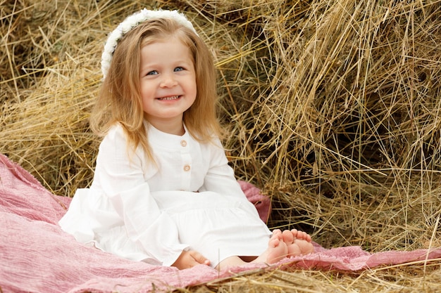 Little girl smiling in a white dress on the hay