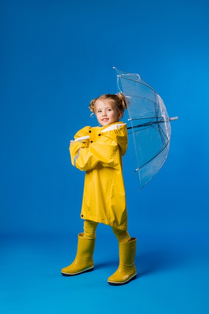 Little girl smiling in a yellow raincoat and rubber boots holding an umbrella