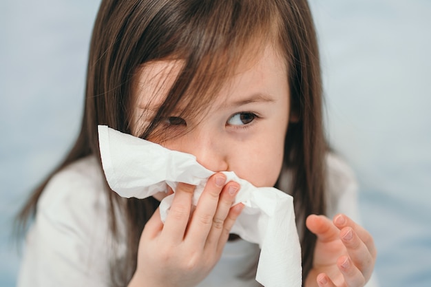 A little girl sneezes. The child has a cold and is being treated at home. The girl is lying in a bed with blue bed linen