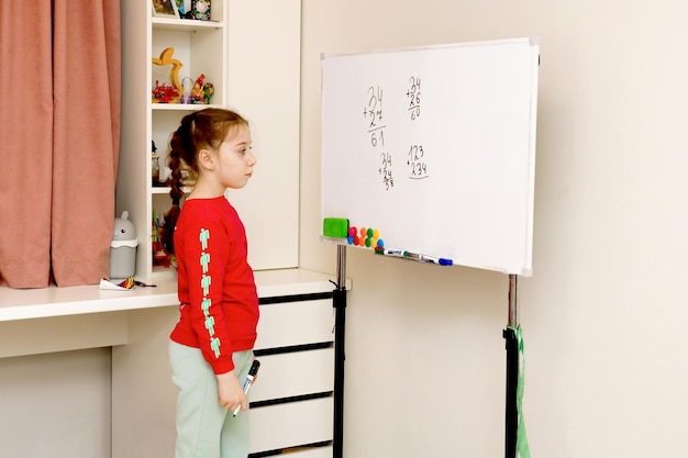 Photo little girl solves house examples on the blackboard