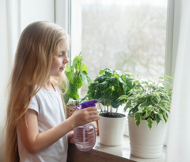 Bambina che spruzza acqua sulle piante d'appartamento