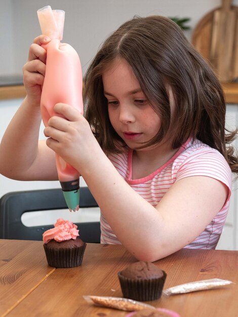 어린 소녀가 요리 가방에서 컵케이크에 크림을 짜냅니다.