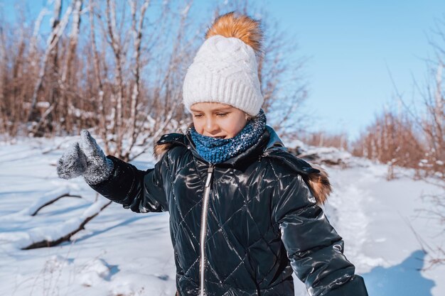 A little girl squints from the sun and runs through a snowy forest in winter