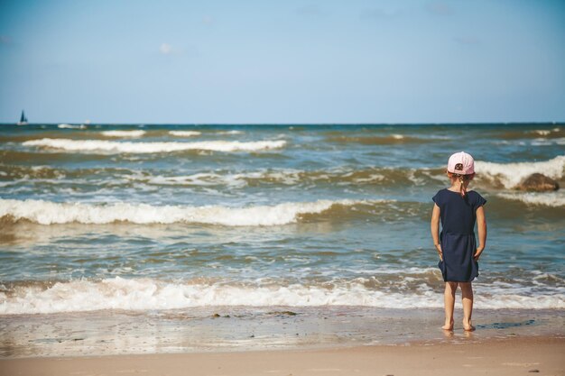 Little girl standing alone watching the waves on the beach of a Baltic sea