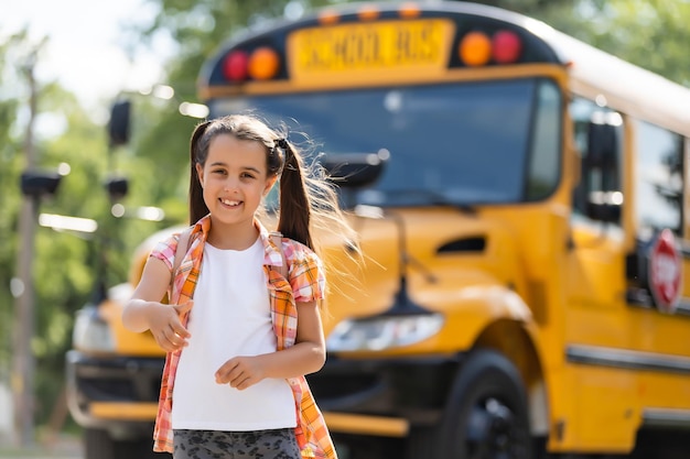 Bambina in piedi vicino a una grande porta dello scuolabus con il suo zaino.