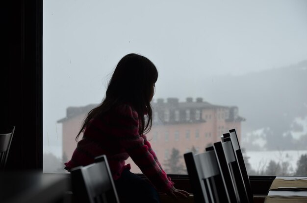 Photo little girl  standing by window against sky