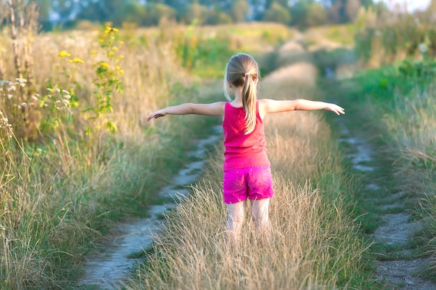 Little girl standing on a field road on a summer sunset evening