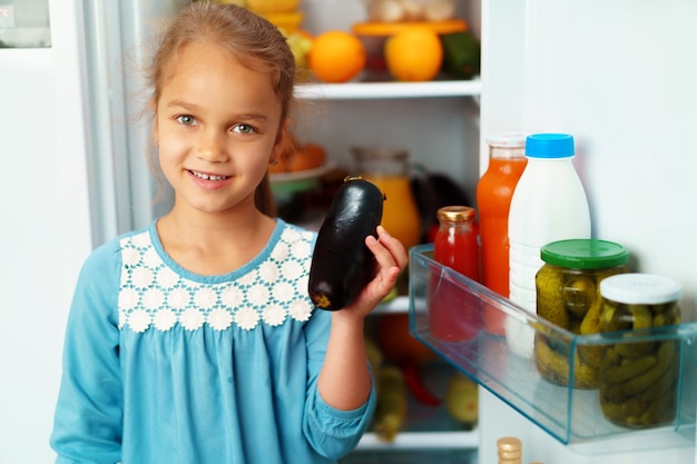 Маленькая девочка стоит перед холодильником и выбирает еду