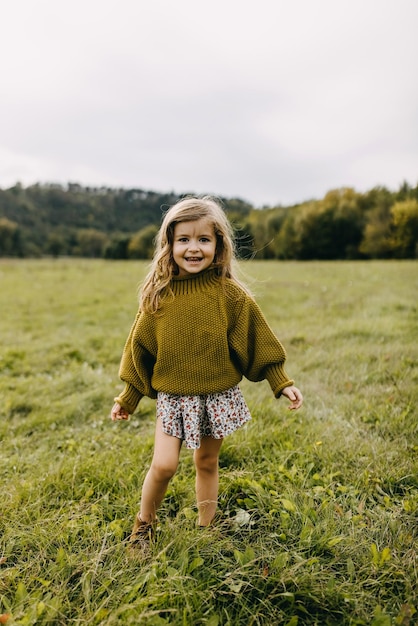 Little girl standing and laughing in an open field with green grass wearing a dress and a sweater