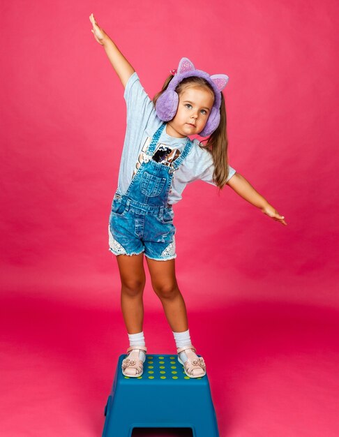 A little girl stands on a chair with her arms outstretched to the sides. isolation on a pink background.