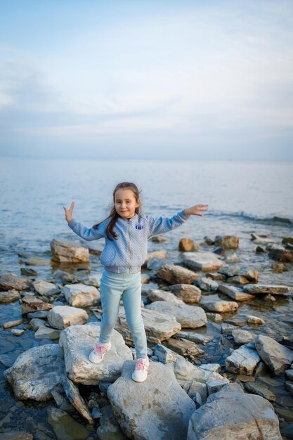 Photo a little girl stands on a large rock on the shore of the sea.