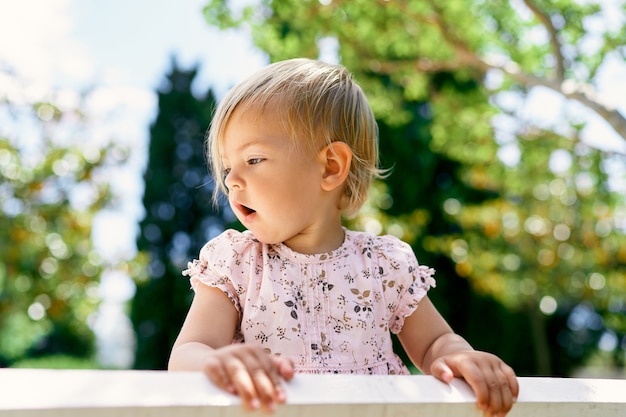 Little girl stands on a park bench turning her head to the side