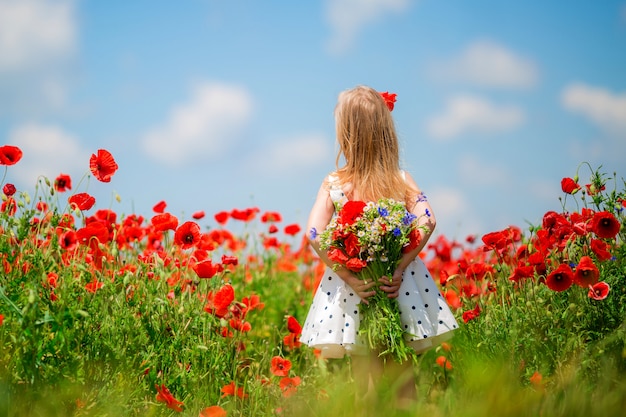 little girl stands with her back in a field of flowers and looks at the sky, the space for text